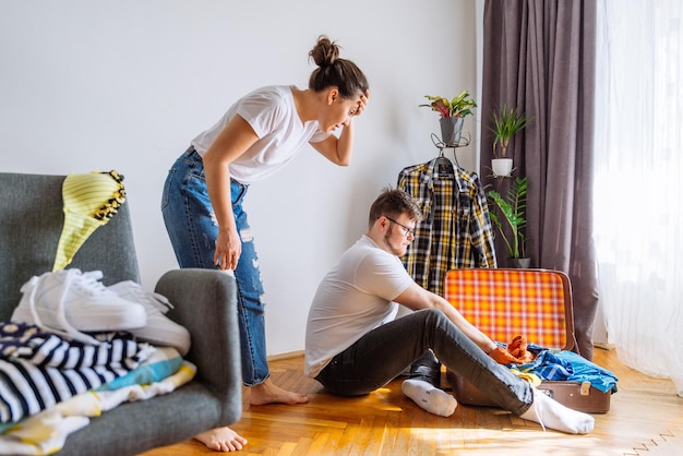 L'uomo ha bisogno dell'aiuto della donna per imballare il concetto di viaggio Uomo che prova i vestiti in forma nella borsa da viaggio