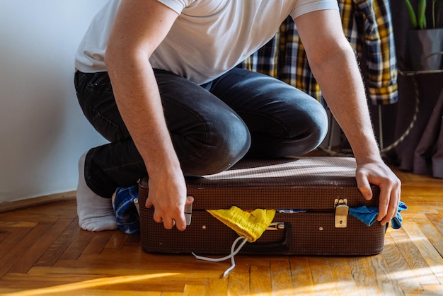 L'uomo ha bisogno di aiuto per chiudere la borsa sovraccaricata della valigia con il concetto di viaggio dei vestiti