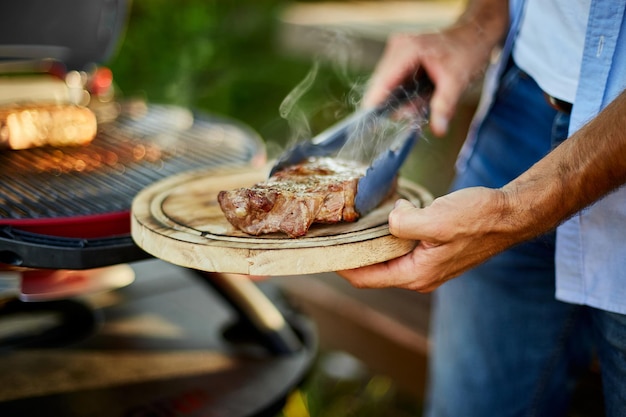 L'uomo ha messo giù la carne su una tavola di legno pronta da mangiare bistecca alla griglia,