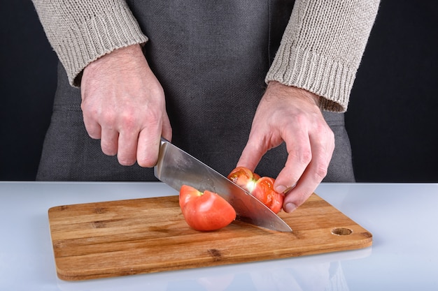 L'uomo ha tagliato un pomodoro in due metà con un coltello.