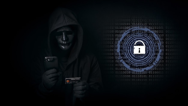 L'uomo hacker con cappuccio e maschera usa smartphone e carta di credito, viola i dati di sicurezza e hackera la password con la chiave sbloccata.