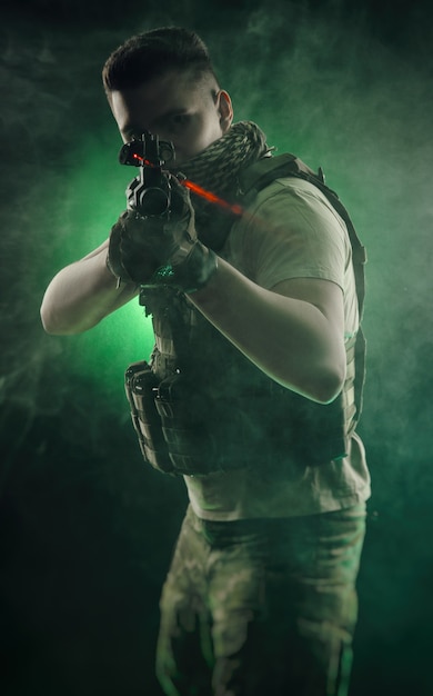 L'uomo in abiti militari speciali in posa con una pistola in mano su uno sfondo scuro nella foschia