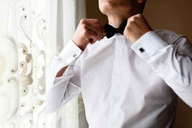 L&#39;uomo in camicia bianca brillante ripara il papillon nero sul collo