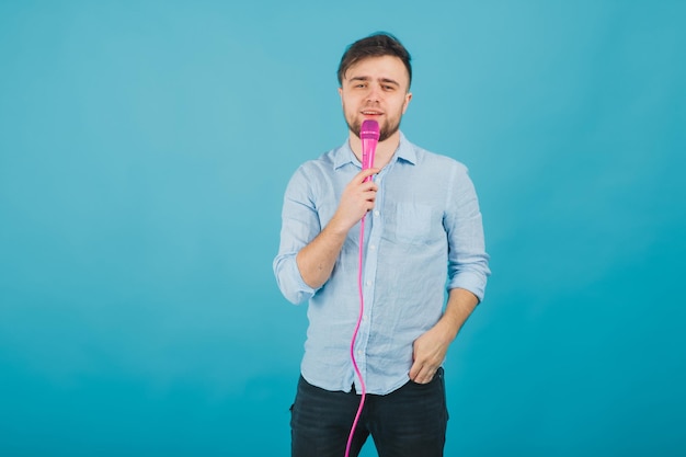 l'uomo in camicia blu sta su sfondo blu e canta con un microfono rosa