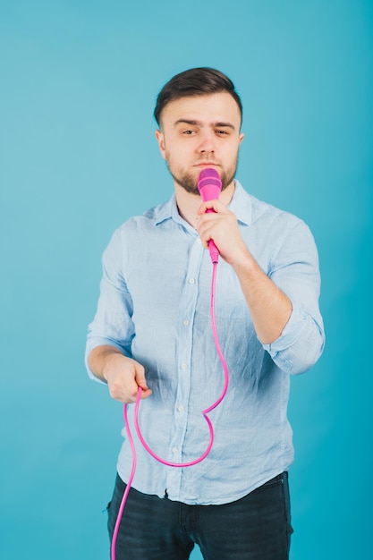 l'uomo in camicia blu sta su sfondo blu e canta con un microfono rosa