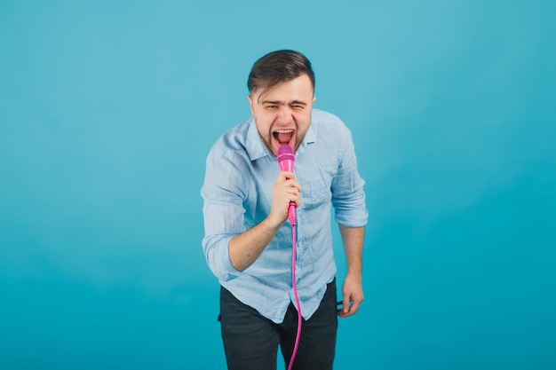 l'uomo in camicia blu sta su sfondo blu e canta con un microfono rosa