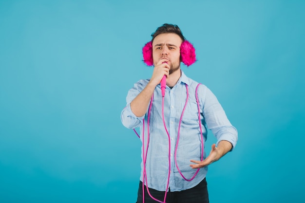 l'uomo in camicia blu sta su sfondo blu in cuffie rosa e canta in microfono rosa