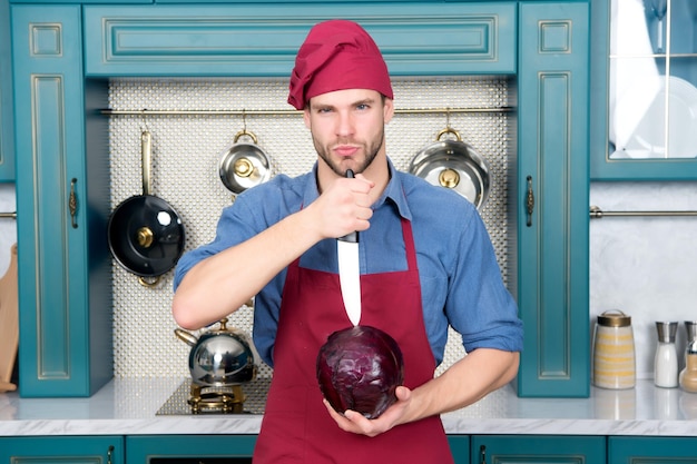 L'uomo in cappello da cuoco rosso ha tagliato il cavolo viola con il coltello