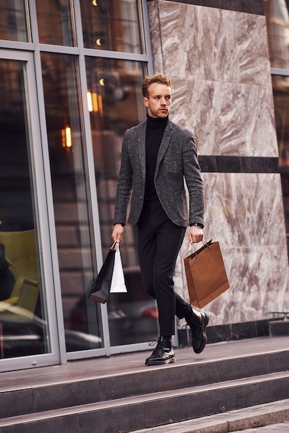 L'uomo in elegante abbigliamento formale e con i pacchetti della spesa è fuori contro un edificio moderno.
