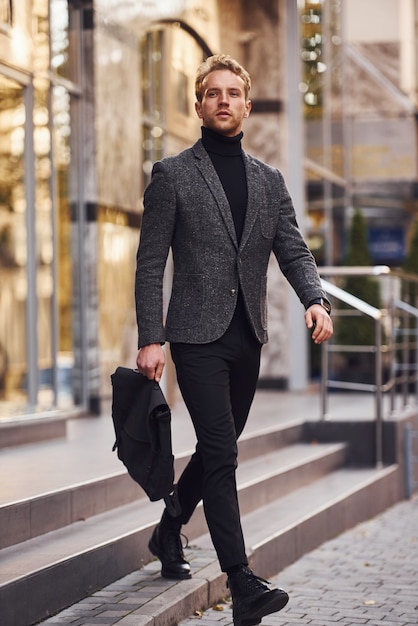 L'uomo in elegante abbigliamento formale e con la borsa è fuori contro un edificio moderno.