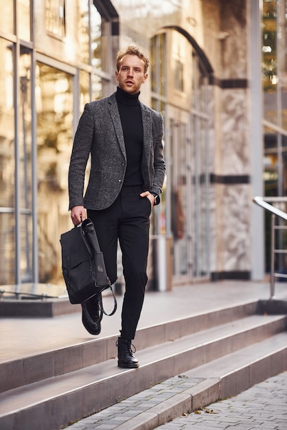 L'uomo in elegante abbigliamento formale e con la borsa è fuori contro un edificio moderno.