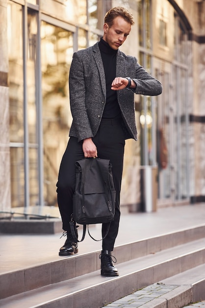 L'uomo in elegante abbigliamento formale e con la borsa è fuori contro un edificio moderno.