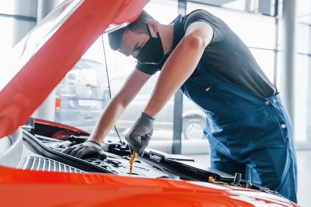 L'uomo in maschera protettiva uniforme e nera lavora con l'automobile rotta. Concezione del servizio auto