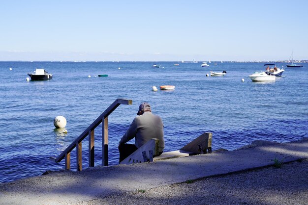 L'uomo in pensione si siede sul porto della costa del mare alla ricerca della costa della spiaggia dell'acqua