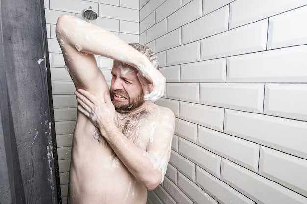 l'uomo in schiuma saponosa si lava sotto la doccia annusa la sua ascella puzzolente ed è disgustato dal corpo non lavato