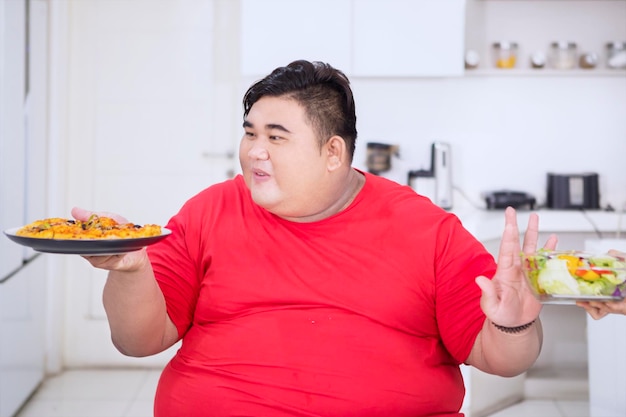L'uomo in sovrappeso mangia la pizza e rifiuta un'insalata