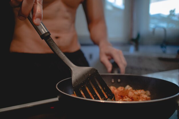L'uomo in topless sta cucinando la sua cena in cucina