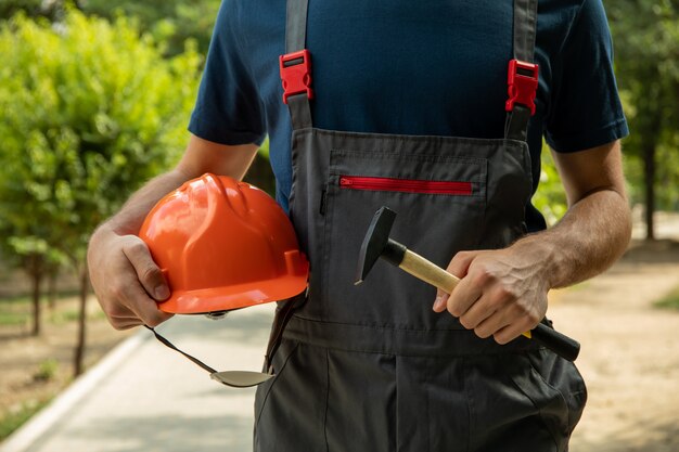 L'uomo in tuta tiene il casco di sicurezza e il martello all'aperto