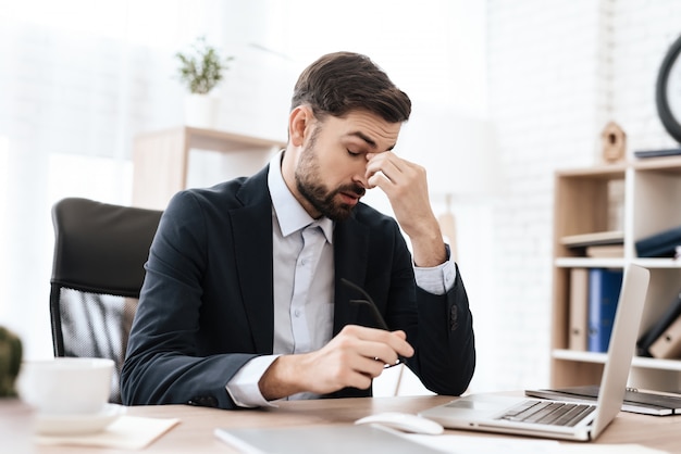 L&#39;uomo in ufficio è seduto e tiene la testa dolorante.