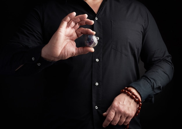L'uomo in una camicia nera tiene una palla di pietra per rituali religiosi