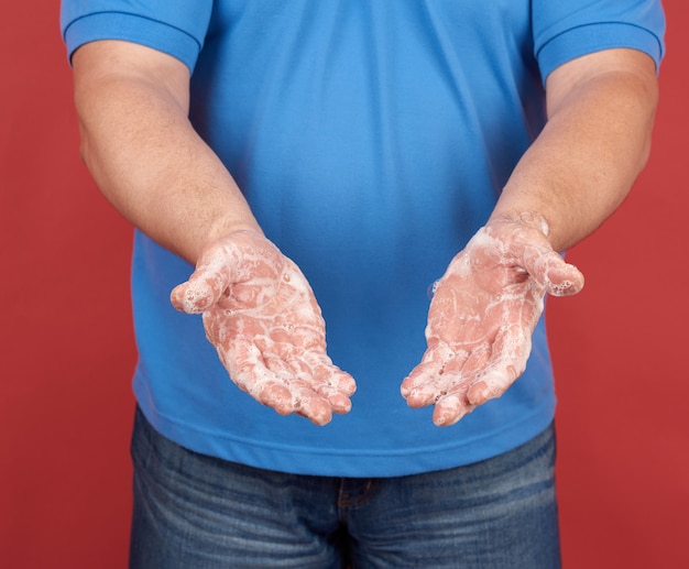 L'uomo in una maglietta blu tiene le mani davanti a una schiuma bianca e sapone