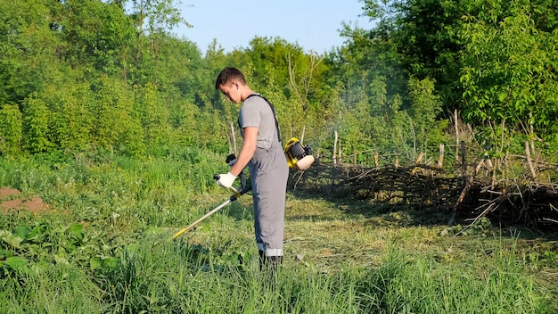 L'uomo in uniforme da lavoro falcia l'erba con un trimmer.