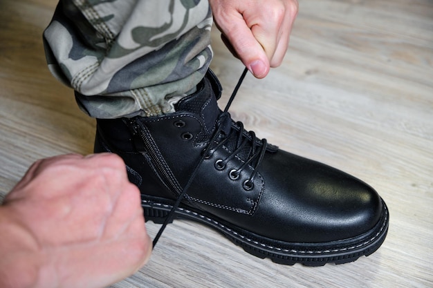 L'uomo in uniforme militare lega i lacci delle sue scarpe nere.