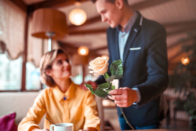 L'uomo in vestito dà fiore di rosa alla giovane donna felice, appuntamento romantico nel ristorante.