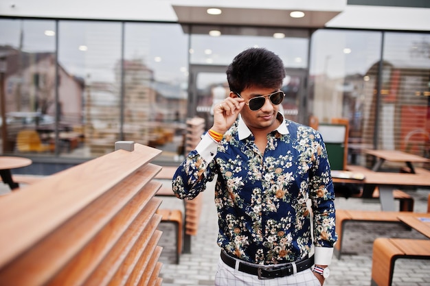 L'uomo indiano alla moda attraente e bello indossa camicia e occhiali da sole in piedi sulla terrazza del moderno lounge cafe durante la sua pausa di lavoro