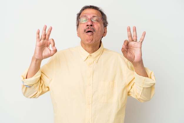 L'uomo indiano di mezza età isolato su sfondo bianco si rilassa dopo una dura giornata di lavoro, sta eseguendo yoga.