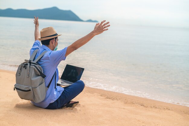 L'uomo indossa la maschera utilizzando il computer portatile sulla spiaggia del mare e l'uomo viaggia in vacanza Phuket sandbox Thailandia sono libertà vita finanziaria