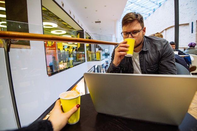 L'uomo lavora sul computer portatile nel centro commerciale Le coppie si siedono nello spazio della copia del caffè delle bevande del caffè