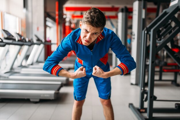 L'uomo magro in abbigliamento sportivo mostra i suoi muscoli, palestra