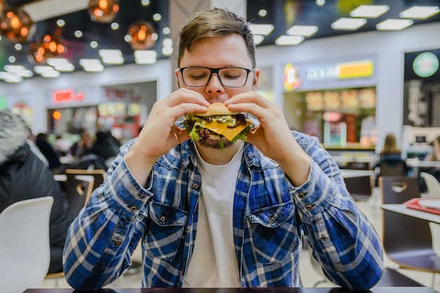 L'uomo mangia hamburger nel caffè del centro commerciale a faccia piena