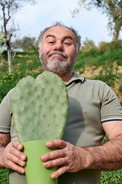 L'uomo maturo barbuto bello tiene un cactus a forma di cuore nel piatto