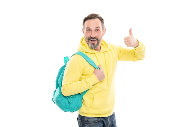 L'uomo maturo felice con barba e baffi in felpa con cappuccio porta la borsa della scuola o lo zaino isolato su bianco mostra il pollice in su alla perfezione
