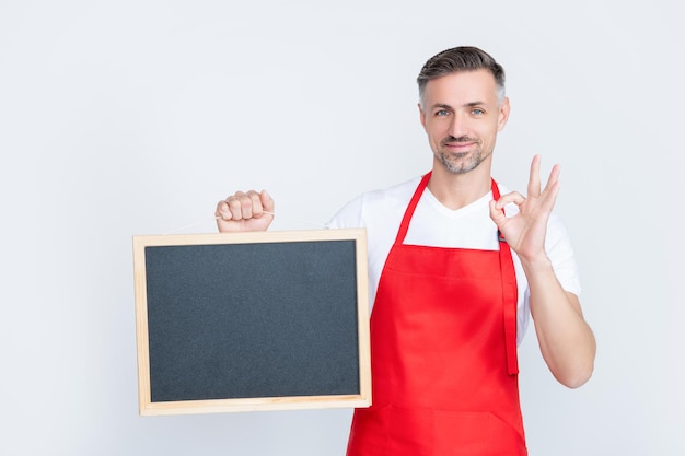 L'uomo maturo positivo in grembiule tiene la lavagna con lo spazio della copia ok