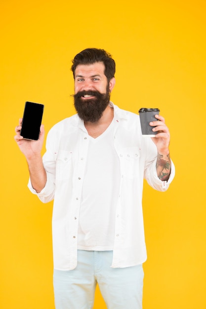 L'uomo maturo sorridente beve il caffè facendo uso del telefono cellulare, routine mattutina.