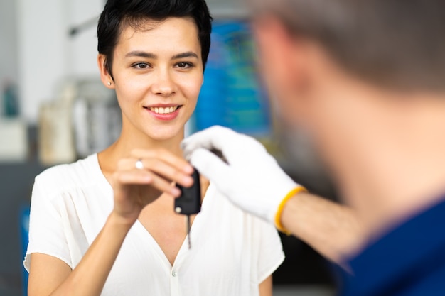 L'uomo meccanico di mezza età con la barba dà la chiave dell'auto al cliente femminile alla stazione di manutenzione dell'auto e al garage di servizio automobilistico