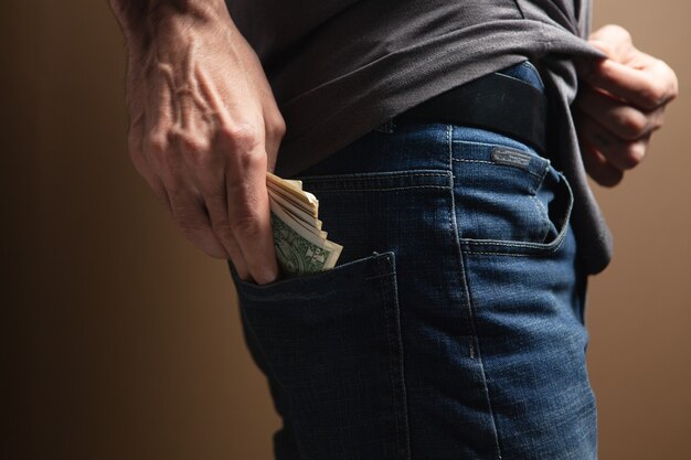 L'uomo mette i soldi nella tasca posteriore su sfondo marrone