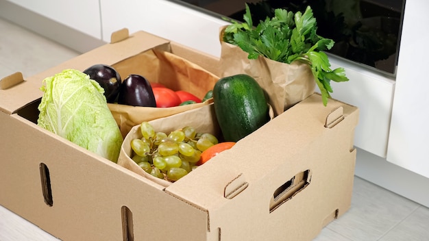 L'uomo mette un contenitore di cartone marrone con varie verdure sul pavimento in cucina in primo piano