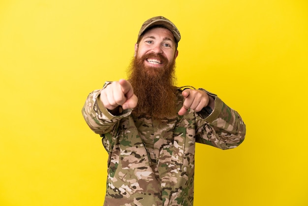 L'uomo militare dai capelli rossi sopra isolato su sfondo giallo punta il dito contro di te mentre sorride