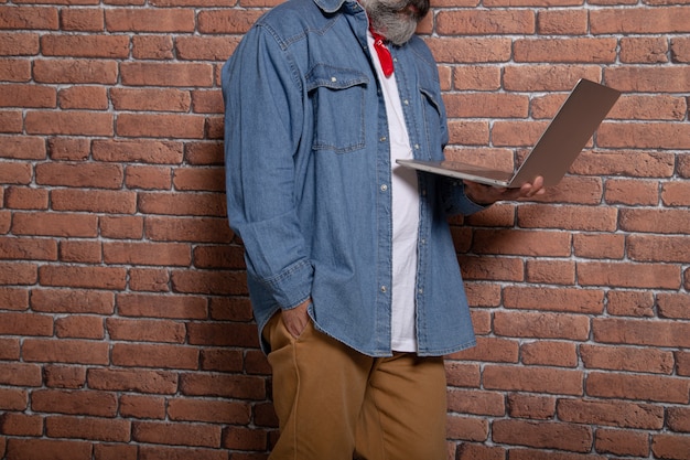 L'uomo moderno che si appoggia sul muro di mattoni tiene un computer portatile. Spazio di coworking