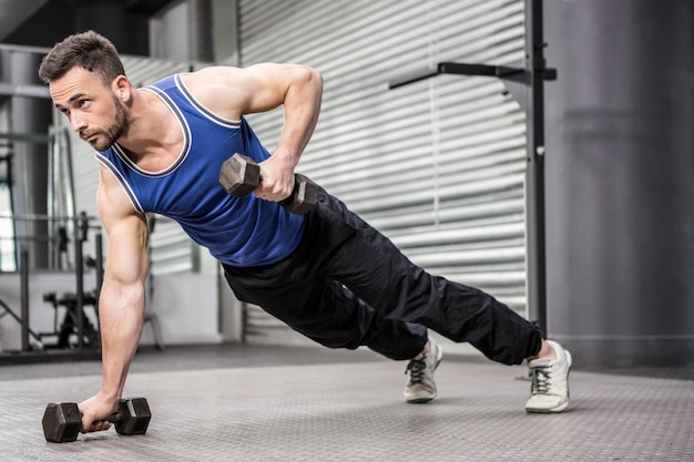 L&#39;uomo muscolare che fa spinge verso l&#39;alto con i dumbbells alla palestra del crossfit