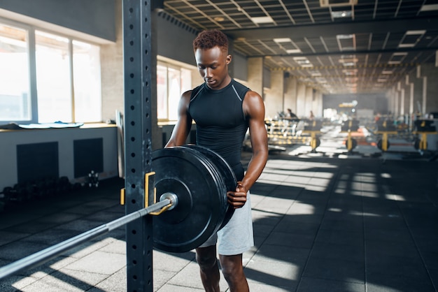 L'uomo muscolare in abiti sportivi prepara il bilanciere sull'allenamento in palestra. Allenamento nel club sportivo, stile di vita sano