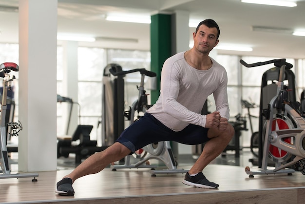 L'uomo muscoloso si allunga sul pavimento in una palestra e flette i muscoli Modello di fitness bodybuilder atletico muscolare