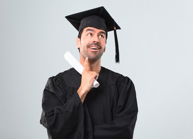 L&#39;uomo nel suo giorno di laurea Università in piedi e pensando un&#39;idea su sfondo grigio