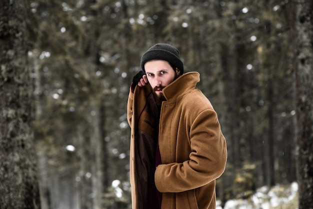 L'uomo nella foresta invernale è freddo e indossa un cappotto marrone e guanti