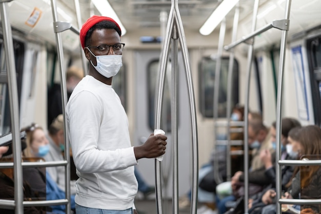 L'uomo nero millenario indossa una maschera per il viso come protezione, tiene il corrimano nel treno della metropolitana attraverso un tovagliolo