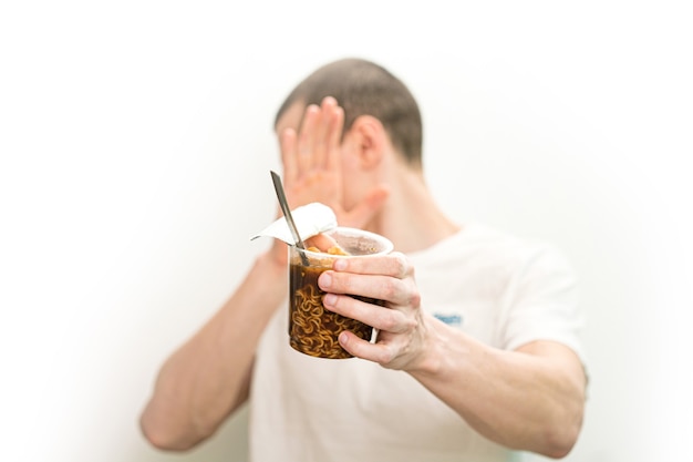 L'uomo non vuole guardare il bicchiere di plastica trasparente di tagliatelle fast food su uno sfondo bianco.